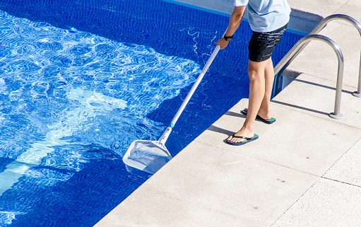Poolservice Person reinigt einen Swimmingpool mit einem Kescher.